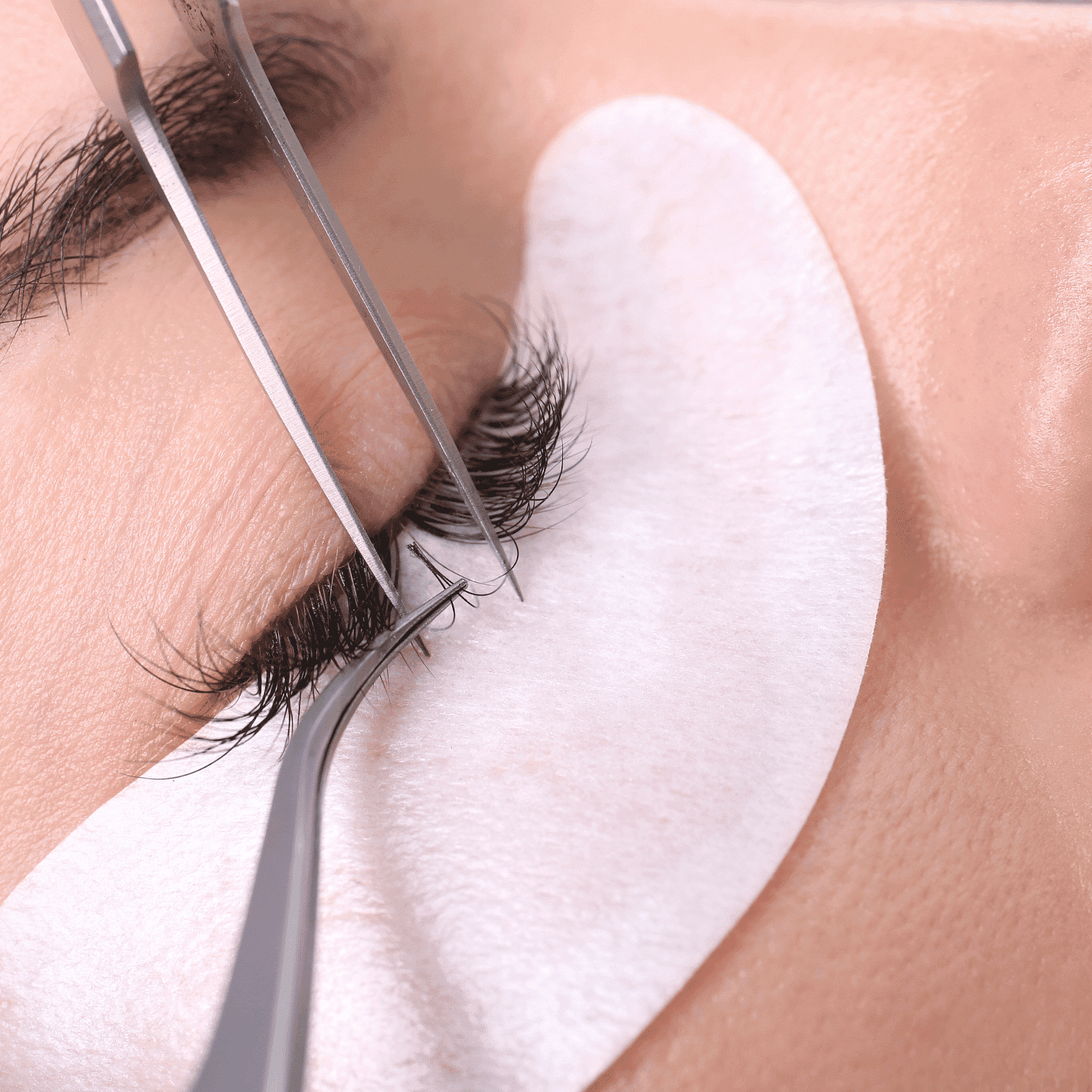 False eyelashes being applied to a person's eyelid with precision tools.