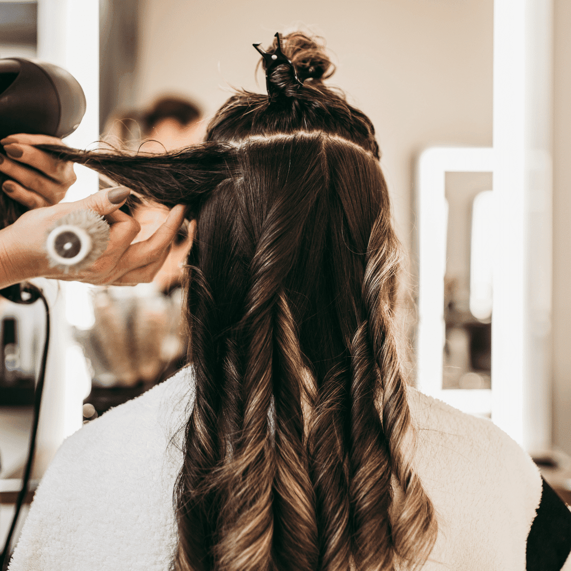 Stylist curling long hair in a salon, preparing it with professional tools.