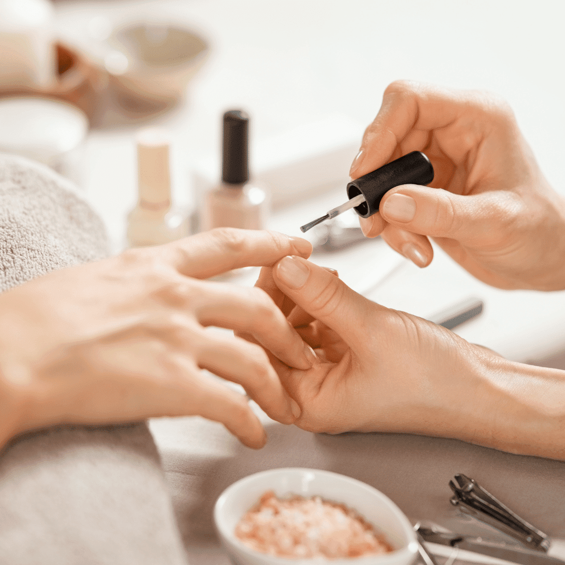 Close-up of a person receiving a manicure, with hands and nail polish bottle in focus.