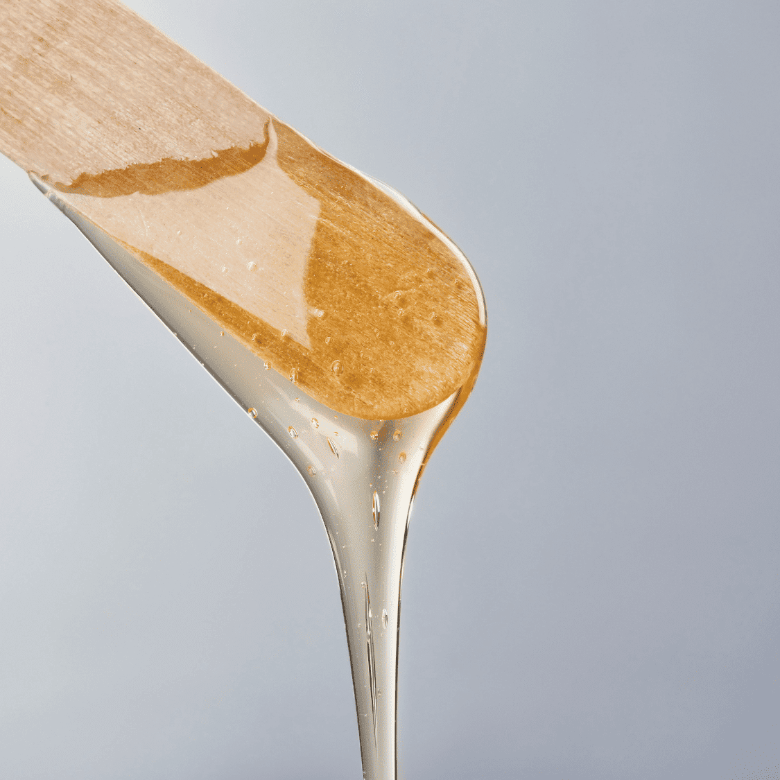 Close-up of honey or syrup dripping from a wooden spatula against a plain background.